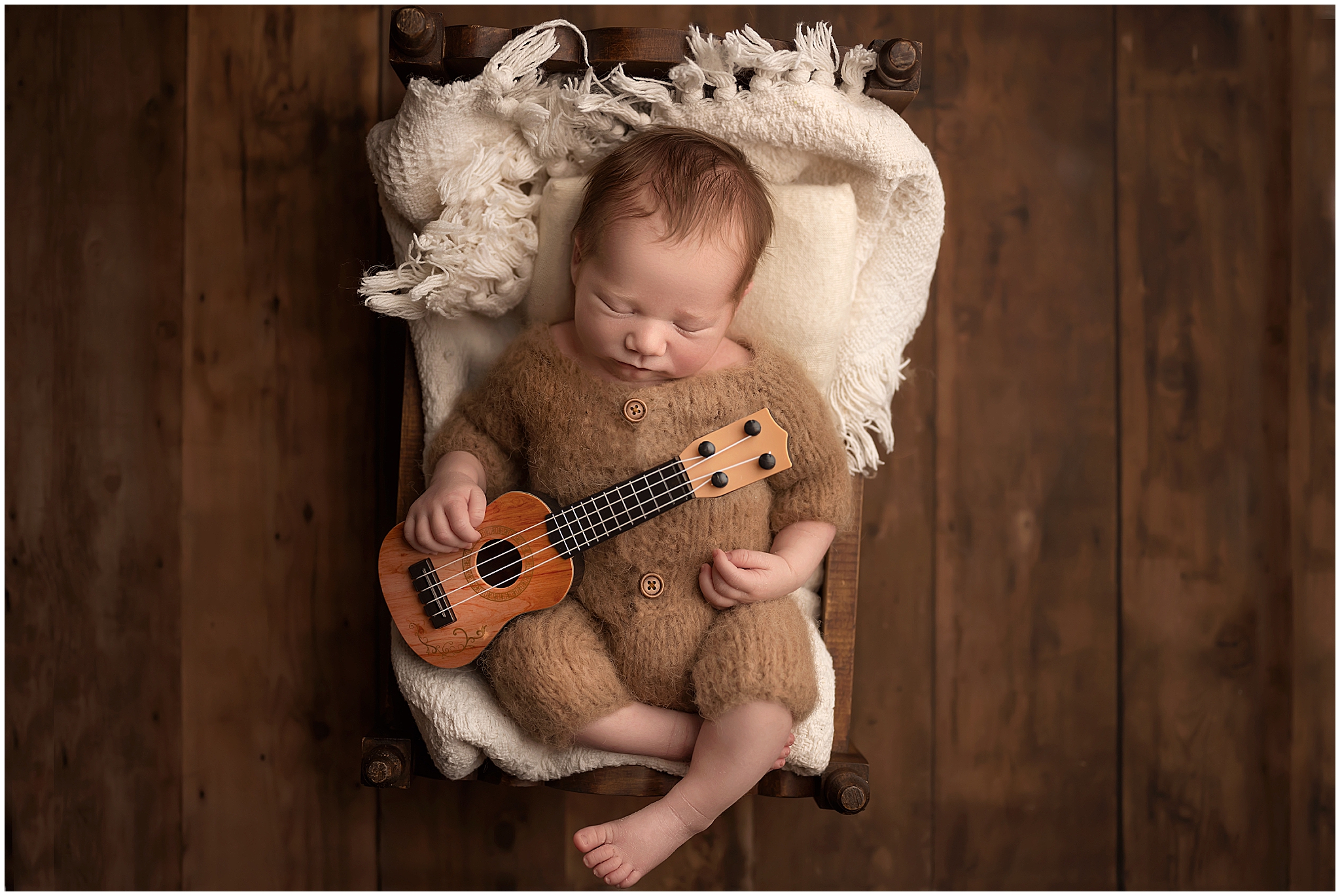 newborn baby sleeping in a small bed holding a tiny guitar 