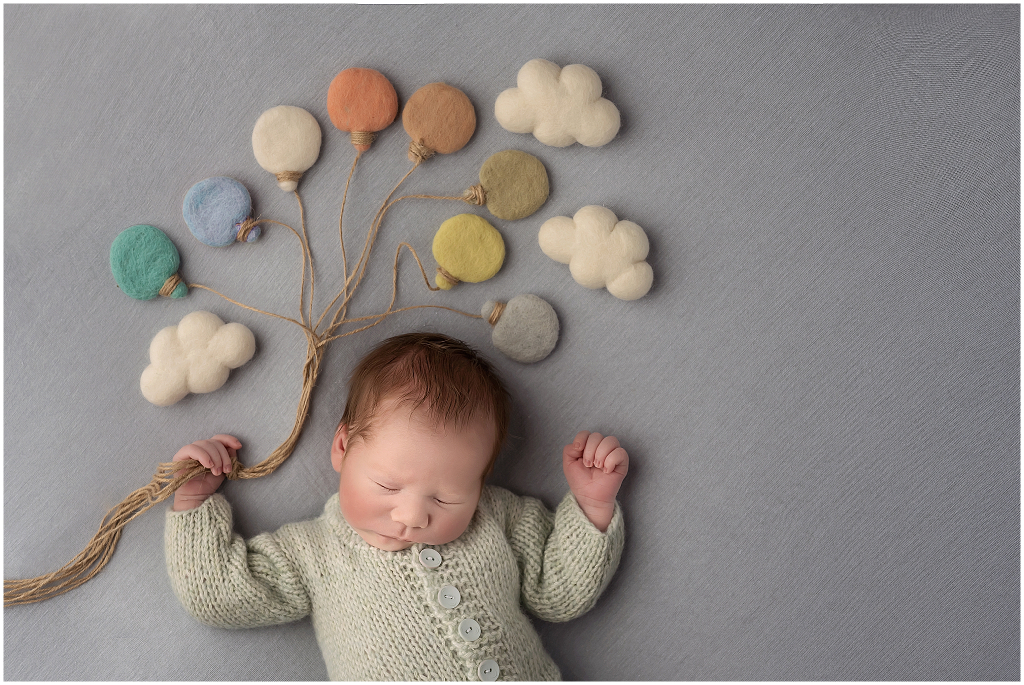 newborn holding felt balloons on light blue backdrop