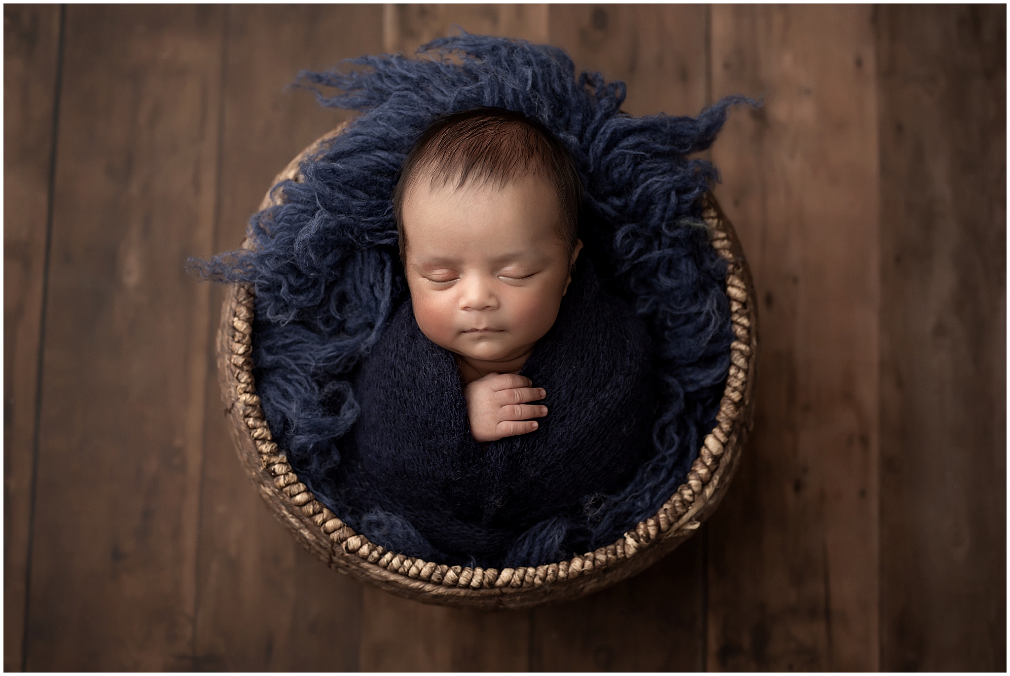 newborn baby boy wrapped and sleeping in baskiet  during newborn photography session at london ontario studio