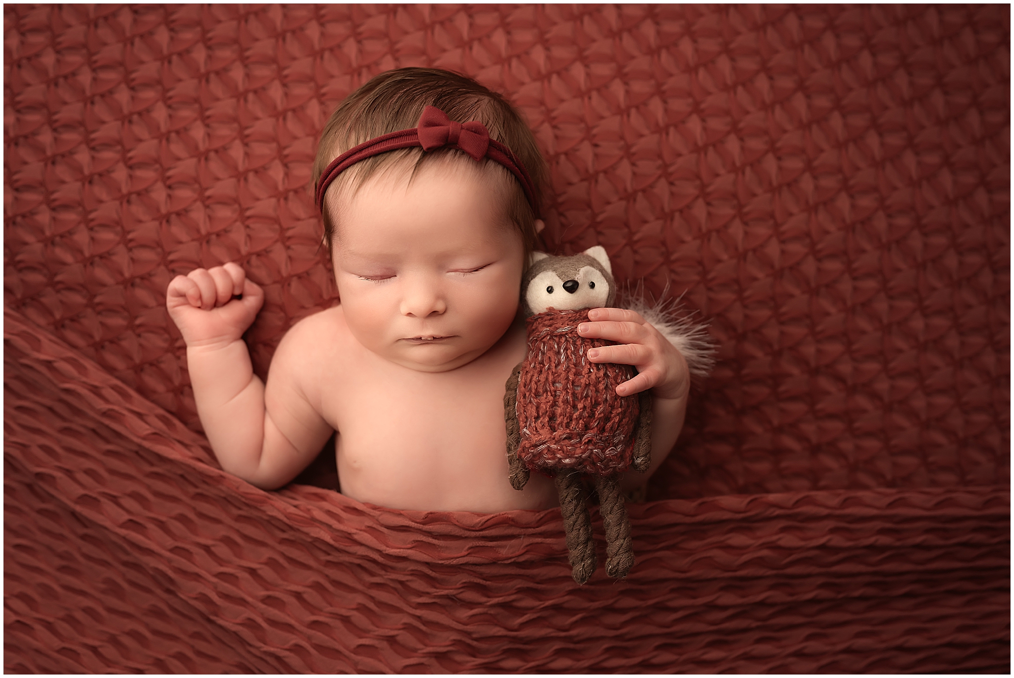 newborn baby girl sleeping with fox on red backdrop during newborn session at london ontario studio